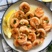 White plate filled with shrimp and a lemon wedge.
