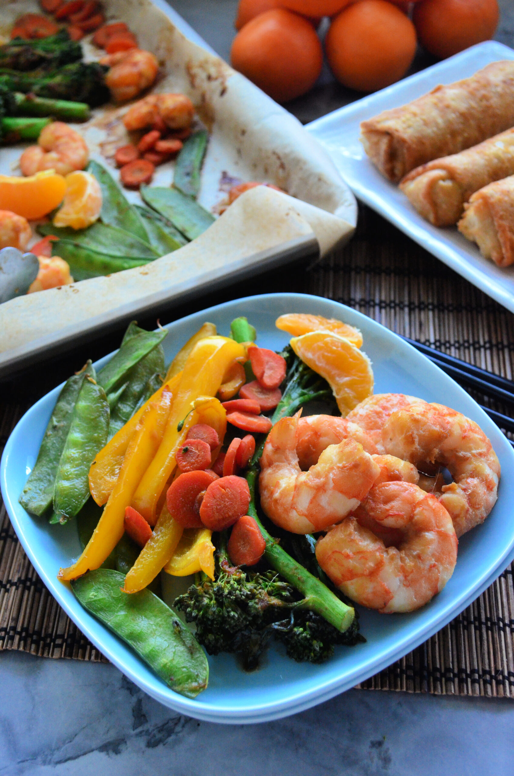 Blue plated filled with veggies and plump shrimp with sheet pan in the background.